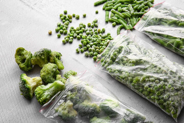 Plastic bags with different frozen vegetables on grey background, closeup