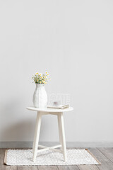 Vase with chamomiles and decor on table near light wall