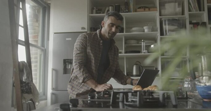 Mid Adult Hispanic Male Using Laptop In Kitchen