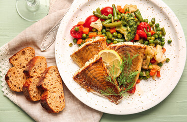 Plate with tasty baked cod fillet, vegetables and bread on color wooden background