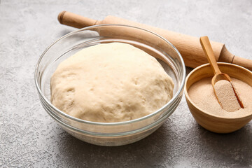 Bowl with fresh dough, dry yeast and rolling pin on light background