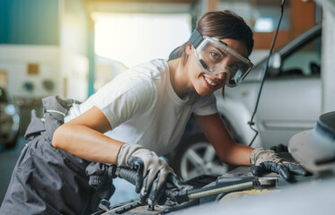 A young latina woman inspects a car engine with a flashlight in a garage. Concept of mechanic woman
