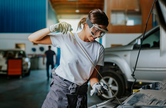 A young woman mechanic checks the oil of a car in a garage. Concept of equality