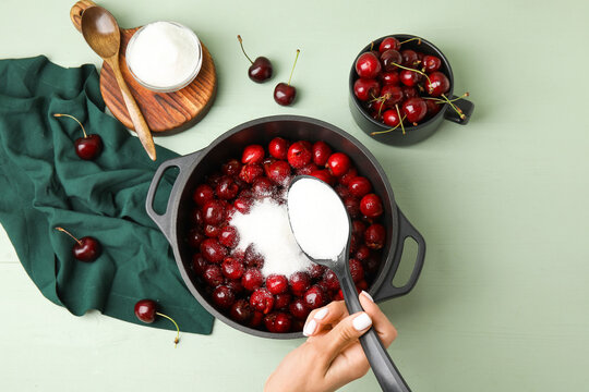Woman preparing sweet cherry jam on color wooden background