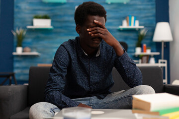 Thoughtful young teenager thinking at university program reflecting management ideas for school course. Stressed african american man sitting on couch in living room contemplating