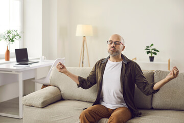 Fototapeta premium Relaxed man meditating on sofa at home. Mature guy sitting on couch, meditating with eyes closed, doing yoga mudra hand gesture, managing stress, enjoying quiet time, feeling calm, peaceful and serene