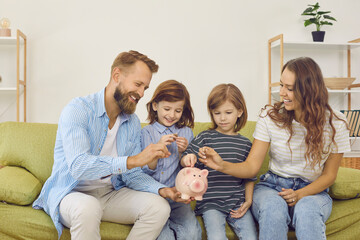 Mom and dad teach their sons to manage their budgets effectively and spend money wisely. Happy parent and their young children put coins in piggy bank sitting on sofa in room. Concept of family budget