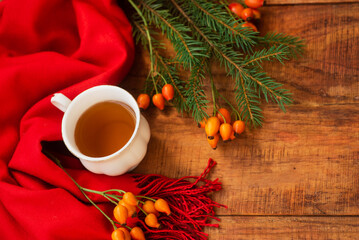 winter, warm atmosphere. A cup of hot black tea with a red scarf, rose berries and spruce on a wooden background