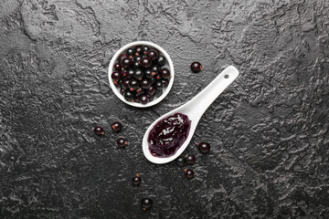 Bowl with berries and delicious black currant jam in spoon on dark background