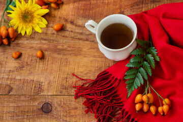 Winter, warm atmosphere. Cup of tea with red scarf, green leafs, rose berries and sunflower on wooden background