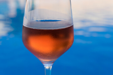 close-up of a wineglass filled with rose wine by the blue water for celebration and romance