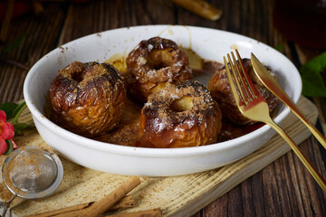 roasted red apples with cinnamon and honey in white earthenware dish on dark wooden table