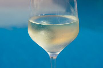 close-up of a wineglass filled with white wine by the blue water for celebration and romance