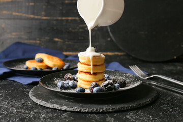 Pouring condensed milk into plate with cottage cheese pancakes on table