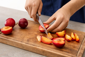 Woman cutting ripe plums at table, closeup