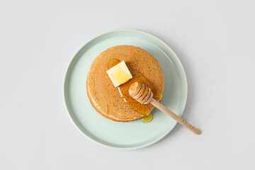 Plate of tasty pancakes with honey and butter on light background