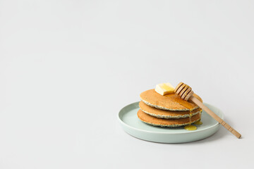 Plate of tasty pancakes with honey and butter on light background