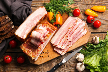 Board with tasty smoked bacon and fresh vegetables on wooden background