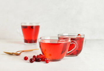 Cups of tasty tea with cranberry on light background