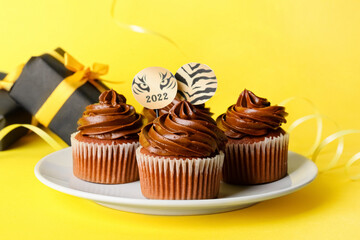 Plate with tasty cupcakes for New Year 2022 celebration on color background