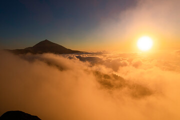 Views of a sunset with the Teide volcano above the clouds and the sun hiding between them.