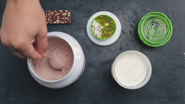 Adding few scoops of chocolate whey protein powder into shaker with milk, slow motion, top view