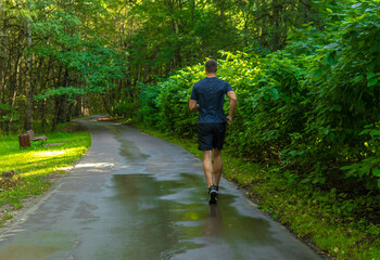 A man athlete runs in the park outdoors, around the forest, oak trees green grass young enduring athletic athlete runner lifestyle outdoor athletic motion, jogging outside. Autumn leisure morning