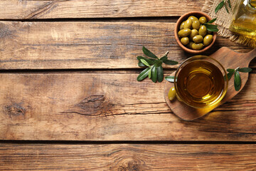 Glass bowl of fresh oil, ripe olives and green leaves on wooden table, flat lay. Space for text