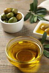 Fresh oil, ripe olives and green leaves on wooden table