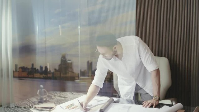 Asian designer standing behind table contemplating and sketching
