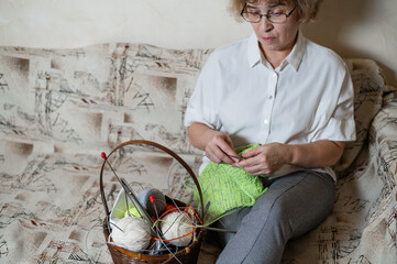 An elderly Caucasian woman knits sitting on a couch.