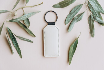 Keychain mockup among olive leaves to display design. Blank white sublimation key chain photo.