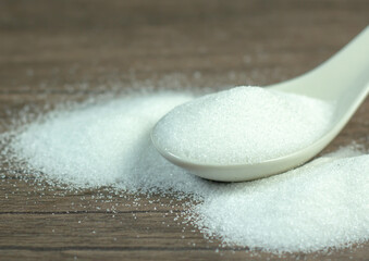 Image close-up sugar-white granulated crystal in spoon white on desk wood for cooking kitchen.