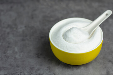 Image close-up sugar-white granulated crystal in a yellow bowl with spoon white on desk wood for cooking kitchen with copy space for text.