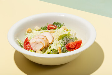 Caesar salad in white plate on yellow hard shadow modern