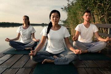 Group of people doing yoga exercises by the lake at sunset.