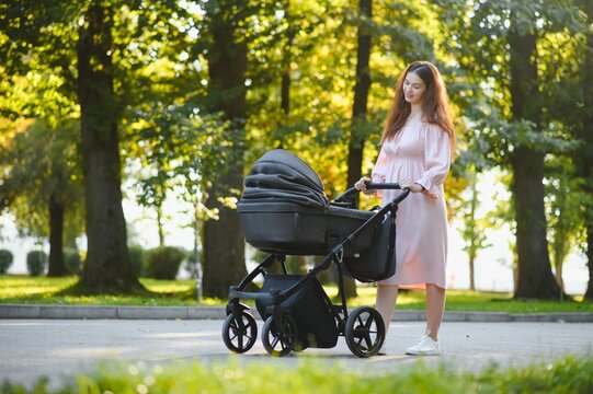 Happy young mother with baby in buggy walking in autumn park