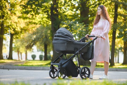 Happy young mother with baby in buggy walking in autumn park