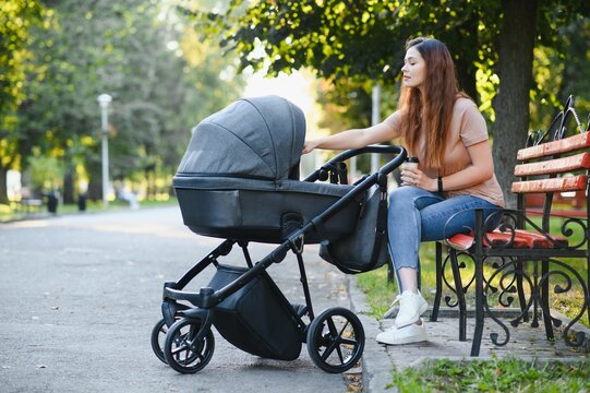 family, child and parenthood concept - happy mother walking with baby stroller in park.