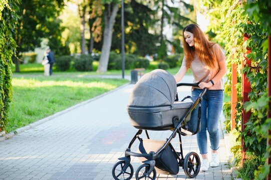 Mum walking on city street. Woman pushing her toddler sitting in a pram. Family concept.