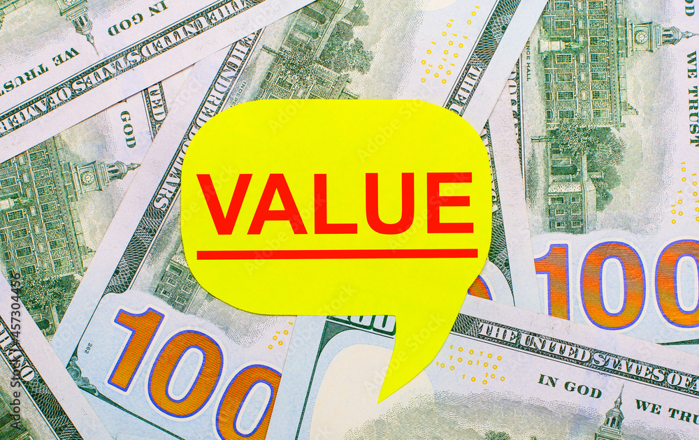 Poster against the background of dollars scattered on the table is a yellow curly card with the text value.