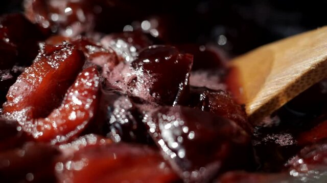 Plum jam is cooked and stirred with a wooden spoon closeup. Shallow depth of field