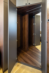 Opened empty wooden wardrobe with mirror inside. Furniture in bedroom.