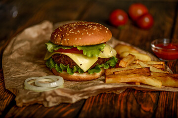 Burger with beef cutlet and potatoes on a wooden background.