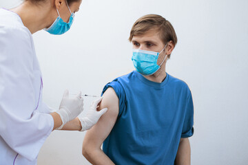 Male getting booster shot Covid-19 vaccine. Doctor making injection to patient in medical mask. Syringe of coronavirus vaccine. Man receives jab vaccinated. Pacents gets a flu shot. Inject in arm  - obrazy, fototapety, plakaty