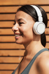 Portrait of African young woman in wireless headphones listening to music and smiling while training outdoors