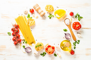 Italian food background on white kitchen table. Raw Pasta, olive oil, spices, tomatoes and basil. Top view with copy space.