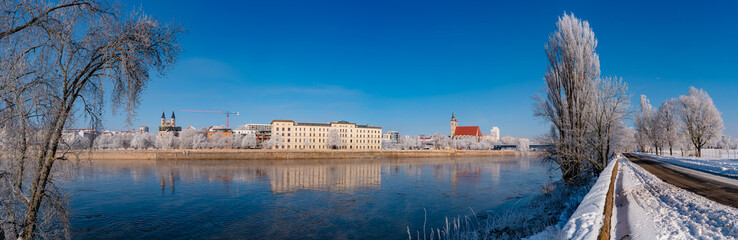 Fototapeta premium Panoramic view over Magdeburg historical downtown in Winter with icy trees and snow during sunrise in the morning with warm illumination and blue sky, Germany.