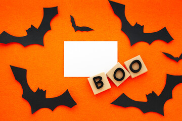 Fototapeta premium Boo word phrase and black bats on orange background. Crafts of the concept of Halloween. Bats, cut out of paper Copy space, place for text. Flat lay top view. Minimal Halloween background.