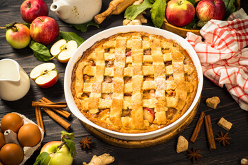 Apple pie with spices at wooden table. Traditional autumn baking with ingredients.